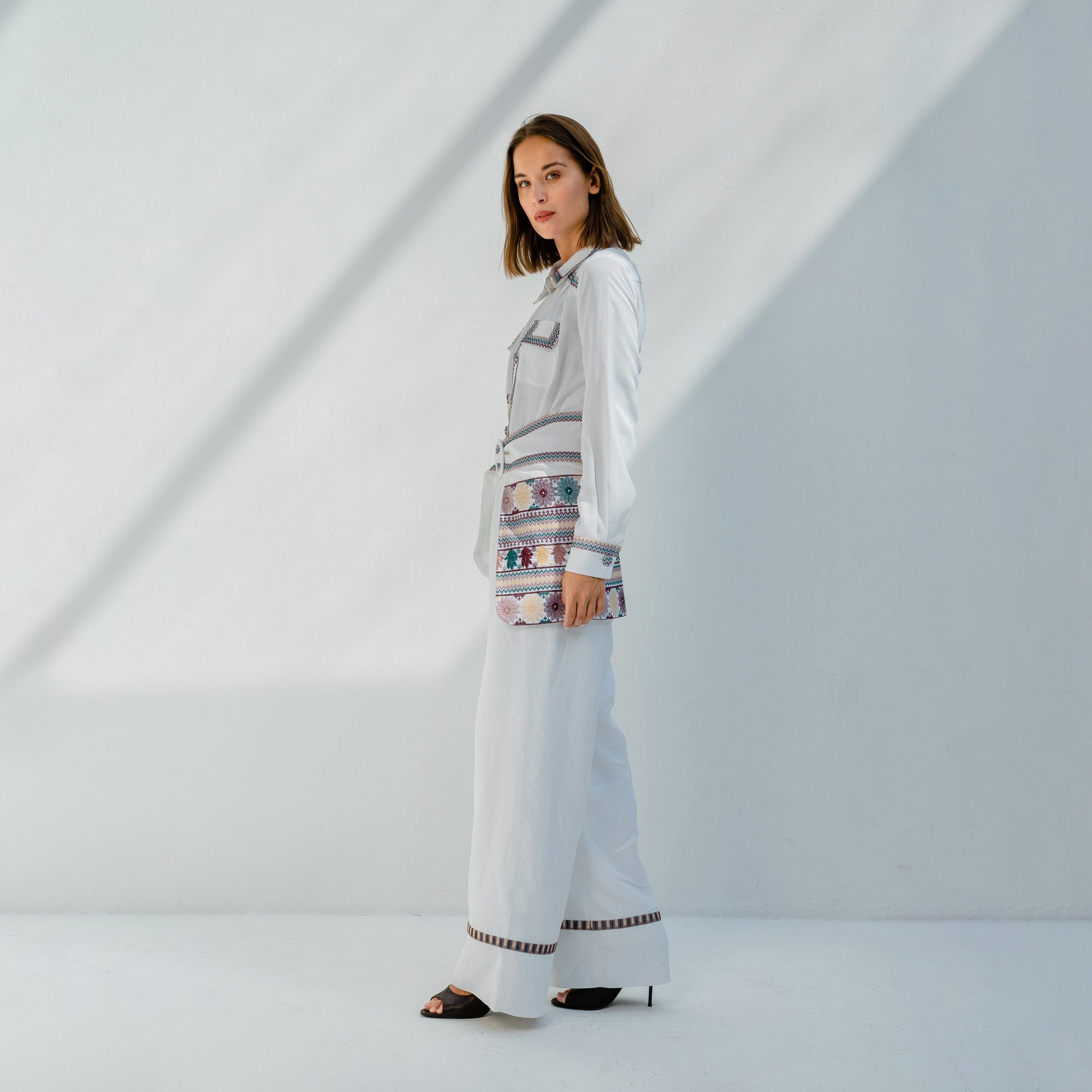 KORONEIKI White Linen Embroidered Long Sleeve Jumpsuit with Separate Waist Belt Piece by Lara Ali